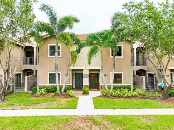Front view of a townhome with two entrances and balconies, surrounded by palm trees.