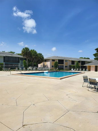 Outdoor view of a swimming pool with chairs and tables around it, located near residential buildings.