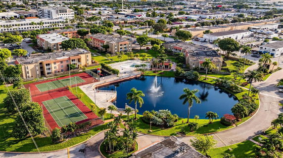 Aerial view of a residential complex with tennis courts and a pond.