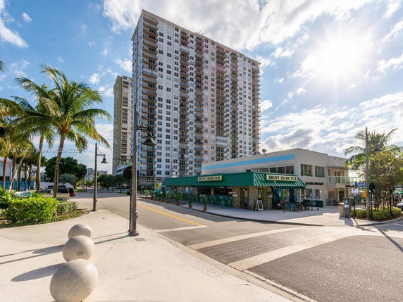 Front view of a high-rise residential building with multiple balconies next to a commercial building with a pub.