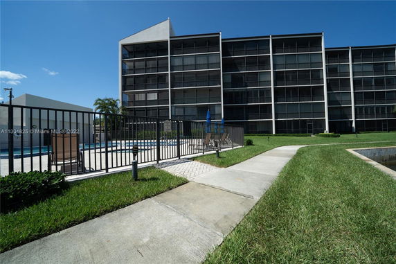 Front view of a multi-story building with balconies and a fenced swimming pool.