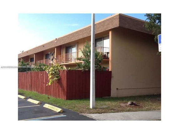 Front view of a two-story apartment building with balconies and a fenced area.