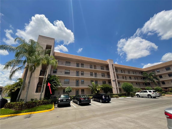 Front view of a multi-story residential building with a parking area and palm trees.