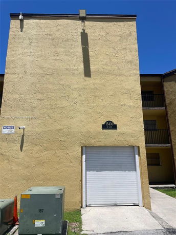 Front view of a building with a yellow textured wall and a white roll-up door.
