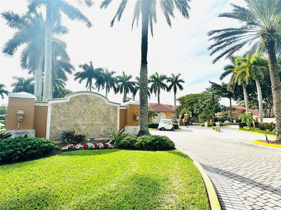 Entrance view of The Enclave luxury condominiums with stone signage and palm trees.