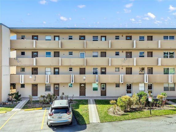 Front view of a multi-story apartment building with balconies and parked cars.
