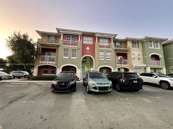 Front view of a multi-story apartment building with balconies and parked cars in front.