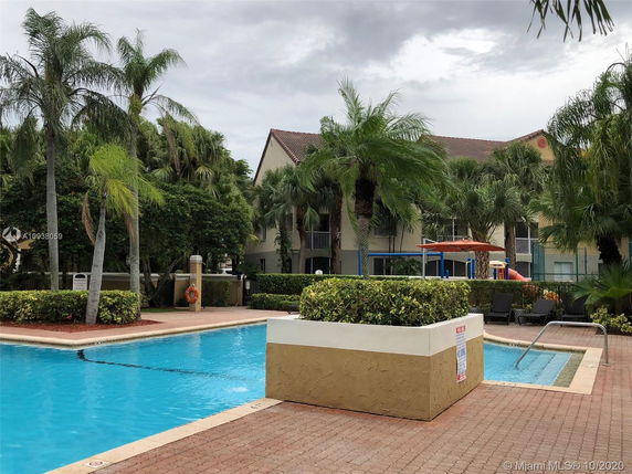 Outdoor swimming pool with a surrounding apartment complex and lush palm trees.