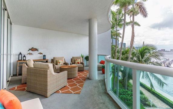 Balcony view with outdoor seating overlooking a waterfront area with palm trees.