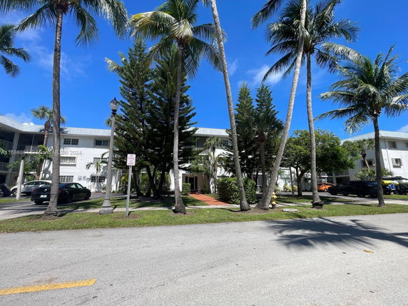 Front view of a residential building with palm trees and parking area.