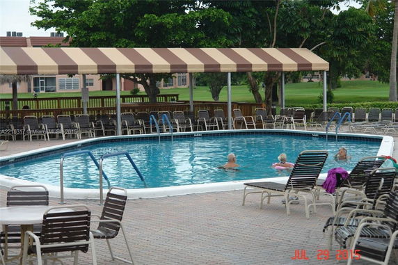 Outdoor swimming pool area with striped canopy and chairs.