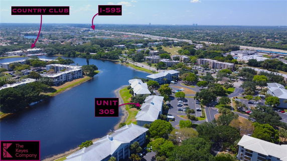 Aerial view of residential buildings near a lake with a road and country club in the background.