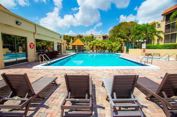 Outdoor swimming pool area with lounge chairs and a small building nearby.