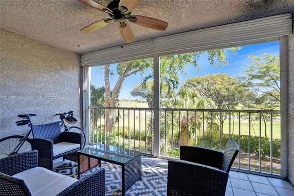 Balcony view with outdoor furniture, ceiling fan, and railing overlooking greenery.