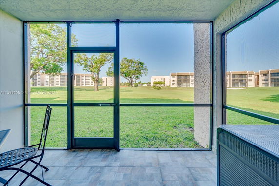 View from a screened patio overlooking grassy lawn and apartment buildings in the background.