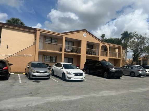 Front view of a two-story apartment building with balconies and parked cars in front.