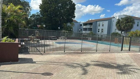 Outdoor swimming pool area with surrounding fence and adjacent buildings.