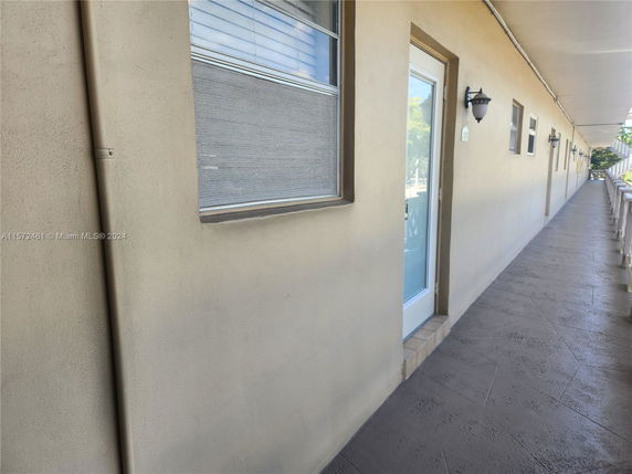 Exterior view of a long corridor outside of a building with multiple doors and windows.