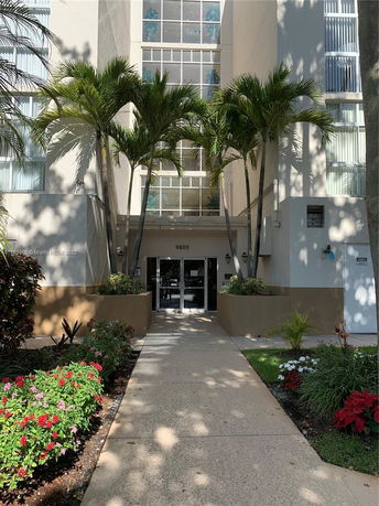 Front view of a multi-story building with a landscaped entrance and large windows.
