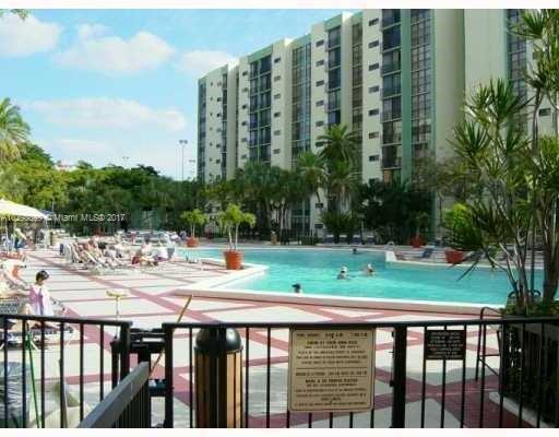 View of a large residential building with a swimming pool area and palm trees in the foreground.