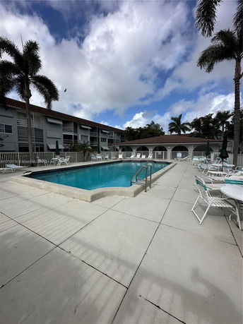 Outdoor swimming pool with surrounding seating area and building in the background.