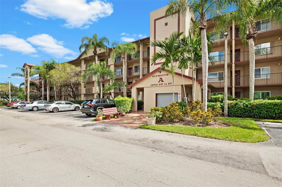 Front view of a multi-story building with balconies and a parking area in front.