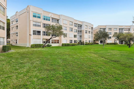 View of a multi-story residential building with a grassy area in front.