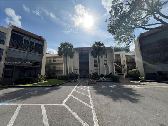 Front view of a multi-story building with palm trees and parking area in front.