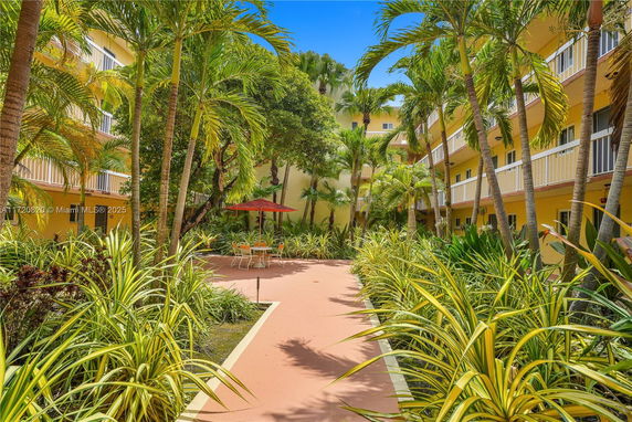 Outdoor view of a multi-story building with balconies surrounded by lush tropical vegetation and a pathway.