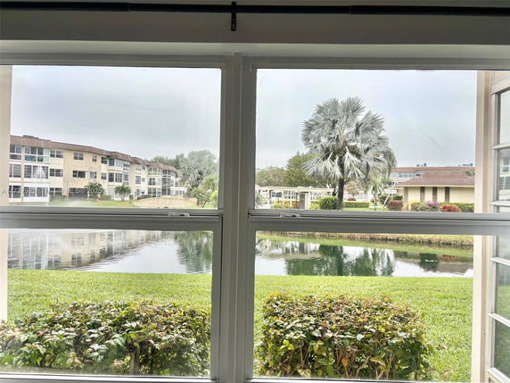 View from a window showing a pond, greenery, and apartment buildings in the background.