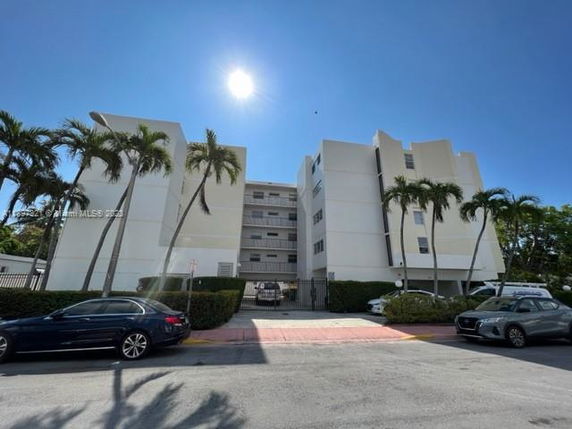Front view of a multi-story white apartment building with palm trees and parked cars.