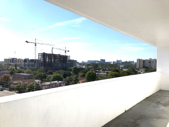 Panoramic view from a balcony, showing a cityscape with construction cranes and buildings in the distance.