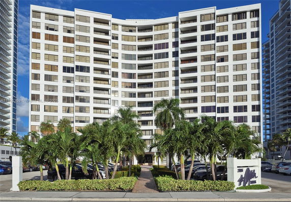Front view of a high-rise residential building with multiple balconies and a central entrance.