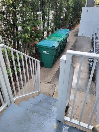 Outdoor view of a staircase leading down to a path with recycling bins beside a building.