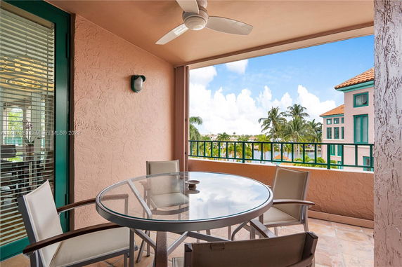 Outdoor balcony with chairs and table, overlooking nearby buildings and palm trees.