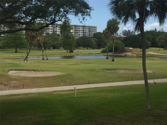 View of a golf course with trees and a building in the background.