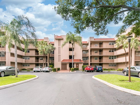 Front view of a multi-story residential building with balconies and a parking area.