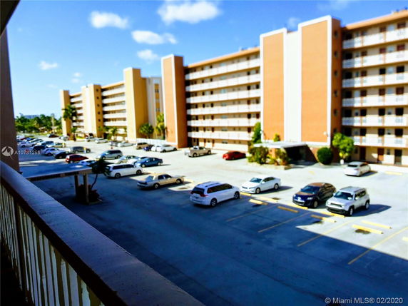 View from a balcony overlooking a multi-story residential building with a parking lot.
