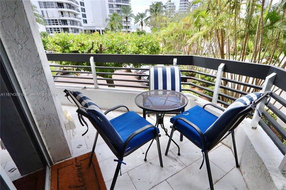 View from a balcony with outdoor chairs and table, overlooking nearby buildings and greenery.