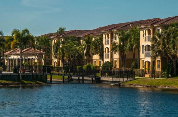 View of a multi-story residential building with a lake and palm trees.