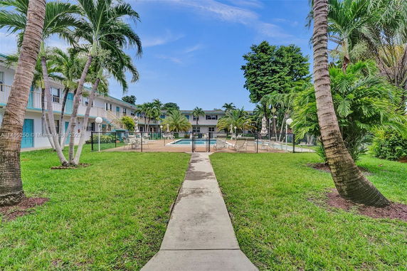 Swimming pool area surrounded by two-story residential buildings and palm trees.