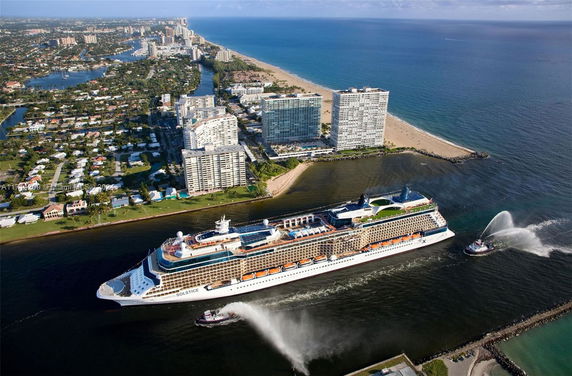 Aerial view showing a cruise ship sailing along a coastline with adjacent urban areas.