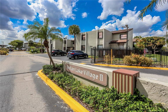 Front view of a residential building complex with a parking area and a sign reading 'Indian Lake Village II'.