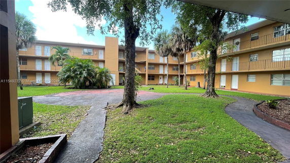 Front view of a three-story apartment building with balconies and green lawn courtyard.