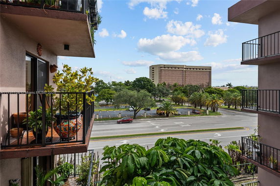 View from a building balcony showing a road and a large building in the distance surrounded by trees.