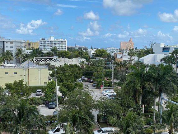 View of multiple buildings surrounded by palm trees and a parking area.