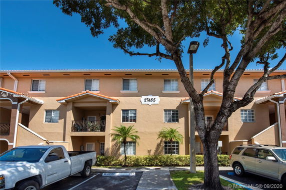 Front view of a multi-story residential building with balconies and parking spaces in front.