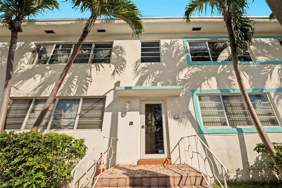 Front view of a two-story building with palm trees and large windows.
