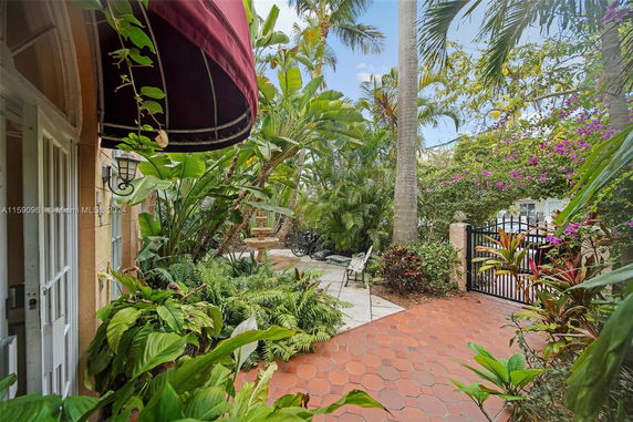 View of a garden area with lush green plants and a tiled pathway adjacent to a building with a red awning.