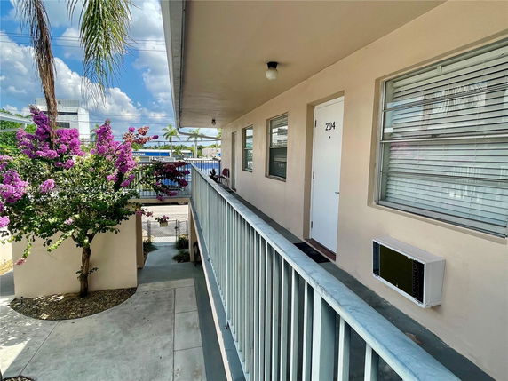 View from a corridor of a building with a door marked 204, overlooking flowering trees and neighboring structures.